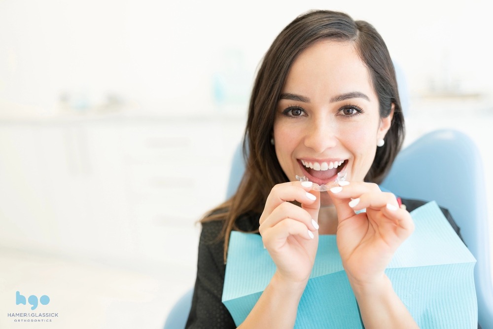 Smiling woman in a dental chair holding a clear aligner after understanding does insurance cover invisalign in charlottesville, VA
