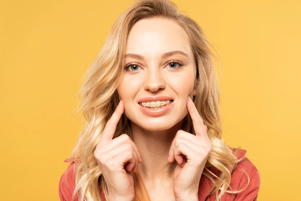 miling blonde woman pointing at her teeth against a yellow background - Overbite vs Underbite in Charlottesville, VA.