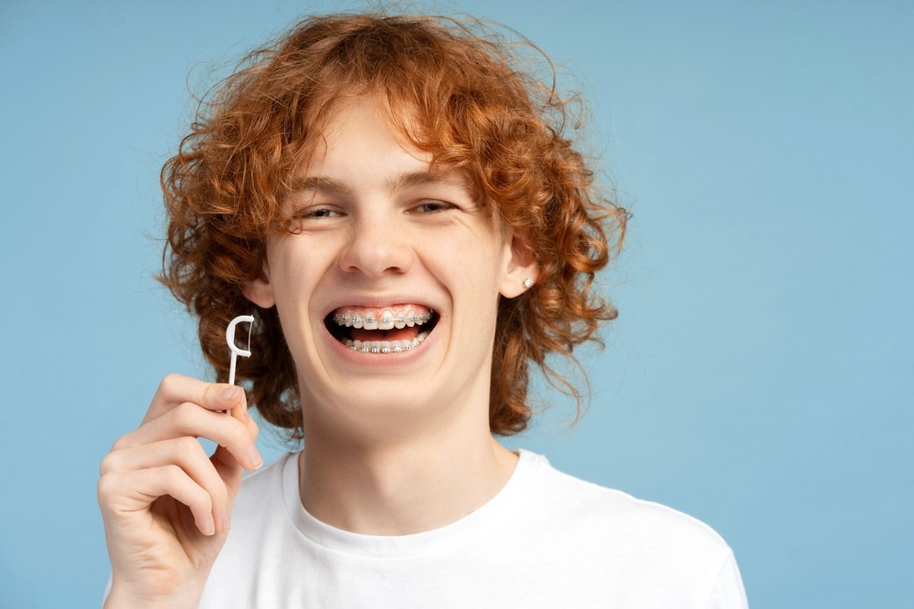 close image smiling teenager curly red hair metal braces - How to Floss with Braces in Charlottesville, VA