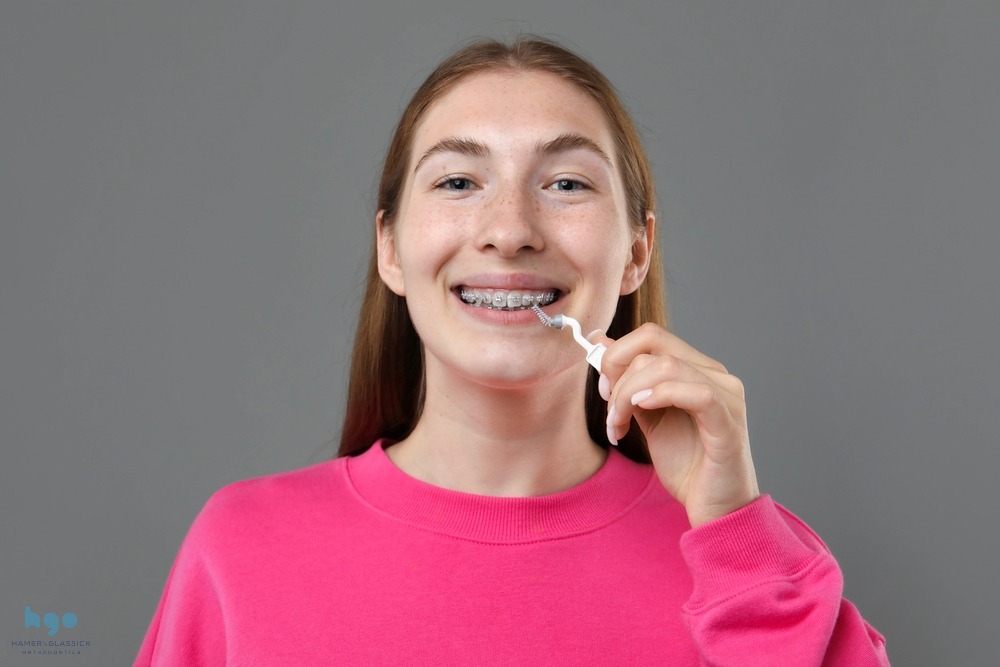 smiling girl metal braces cleaning teeth interdental brush grey background showing How to Floss with Braces in Charlottesville, VA