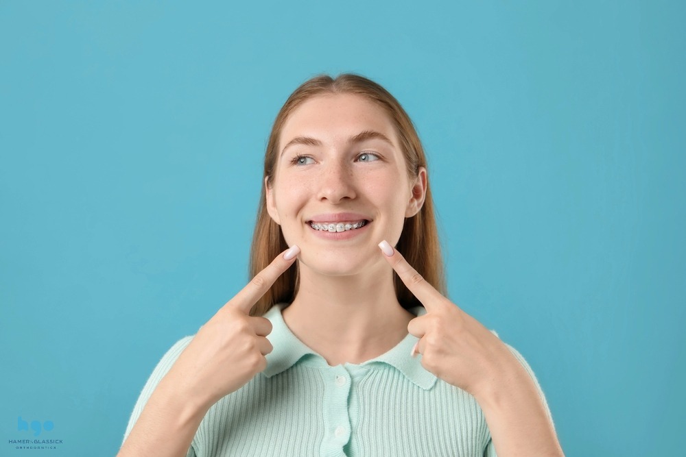 girl pointing her metal braces light blue background - how to clean braces in charlottesville, va