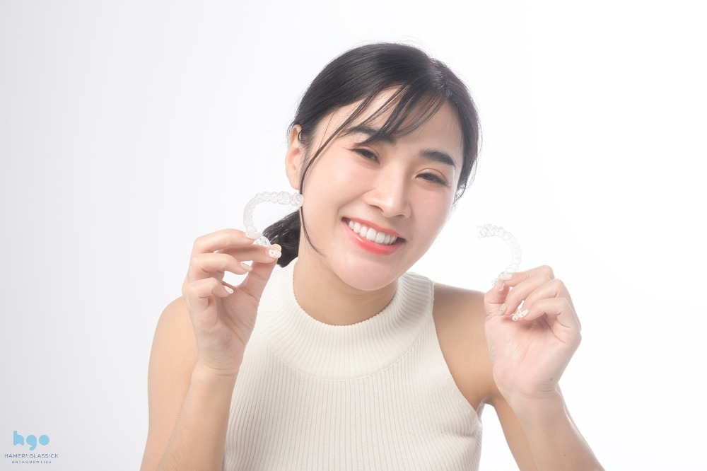 young smiling woman holding invisalign clear aligners white background dental - How Does Invisalign Work in Charlottesville, VA 