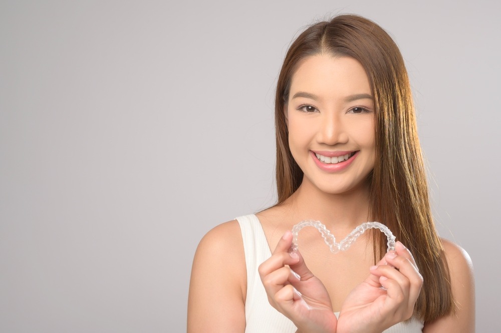 young smiling woman holding invisalign clear aligners white background studio dental - How Does Invisalign Work in Charlottesville, VA